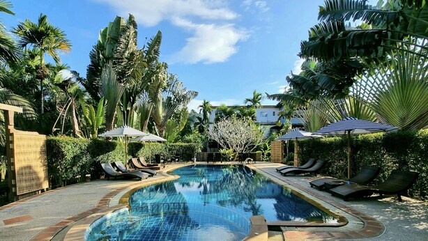 A pool area with lounge chairs and umbrellas, surrounded by tropical plants. - Phuvara Boutique (Krabi)