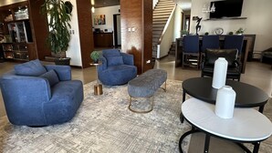 Een moderne woonkamer met een blauwe zithoek, een ronde salontafel en een trap die naar een ander niveau leidt.
