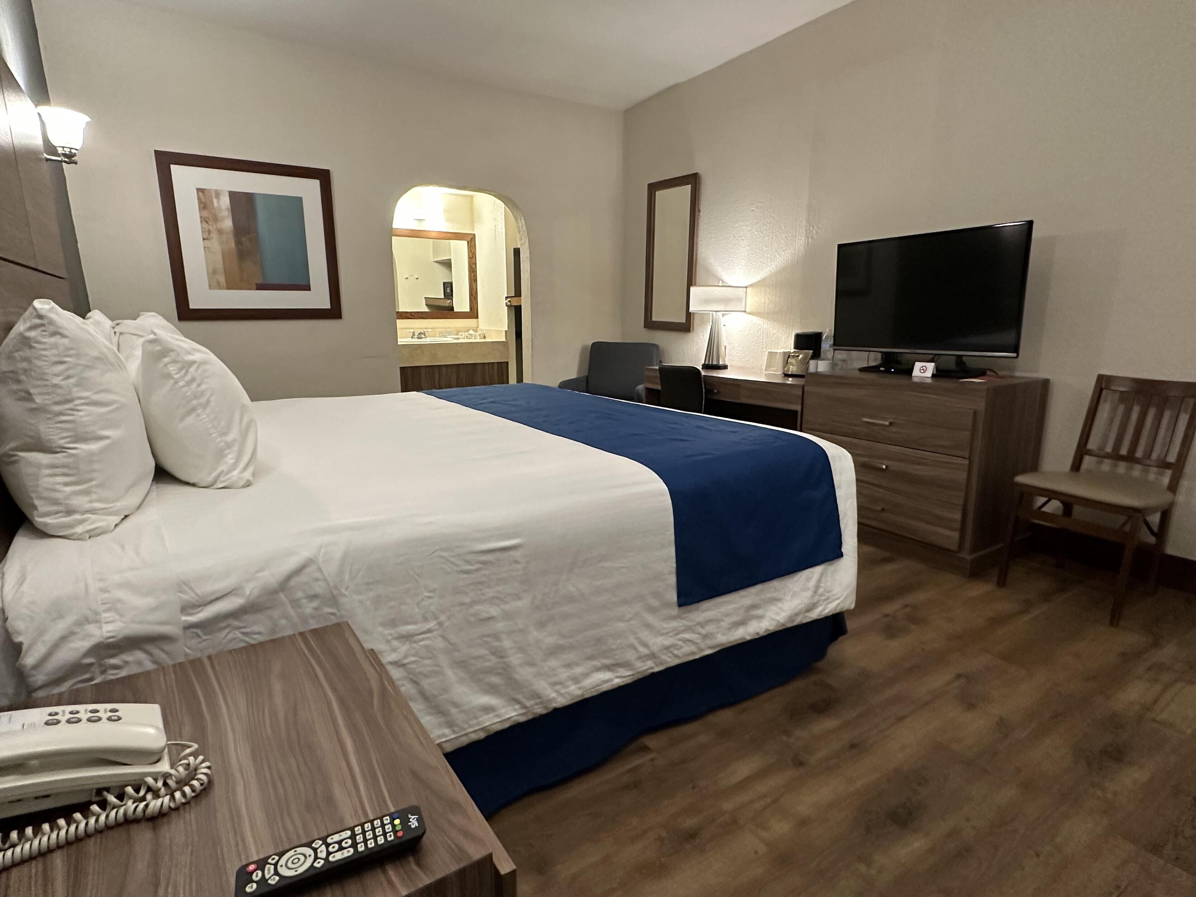 A hotel room with a bed, a desk with a telephone and remote control, a television, a chair, and a dresser.
