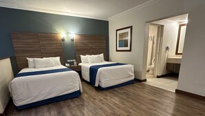 Een hotelkamer met twee bedden, houten vloeren, een nachtkastje met telefoon, en een badkamer die door een open deur zichtbaar is.