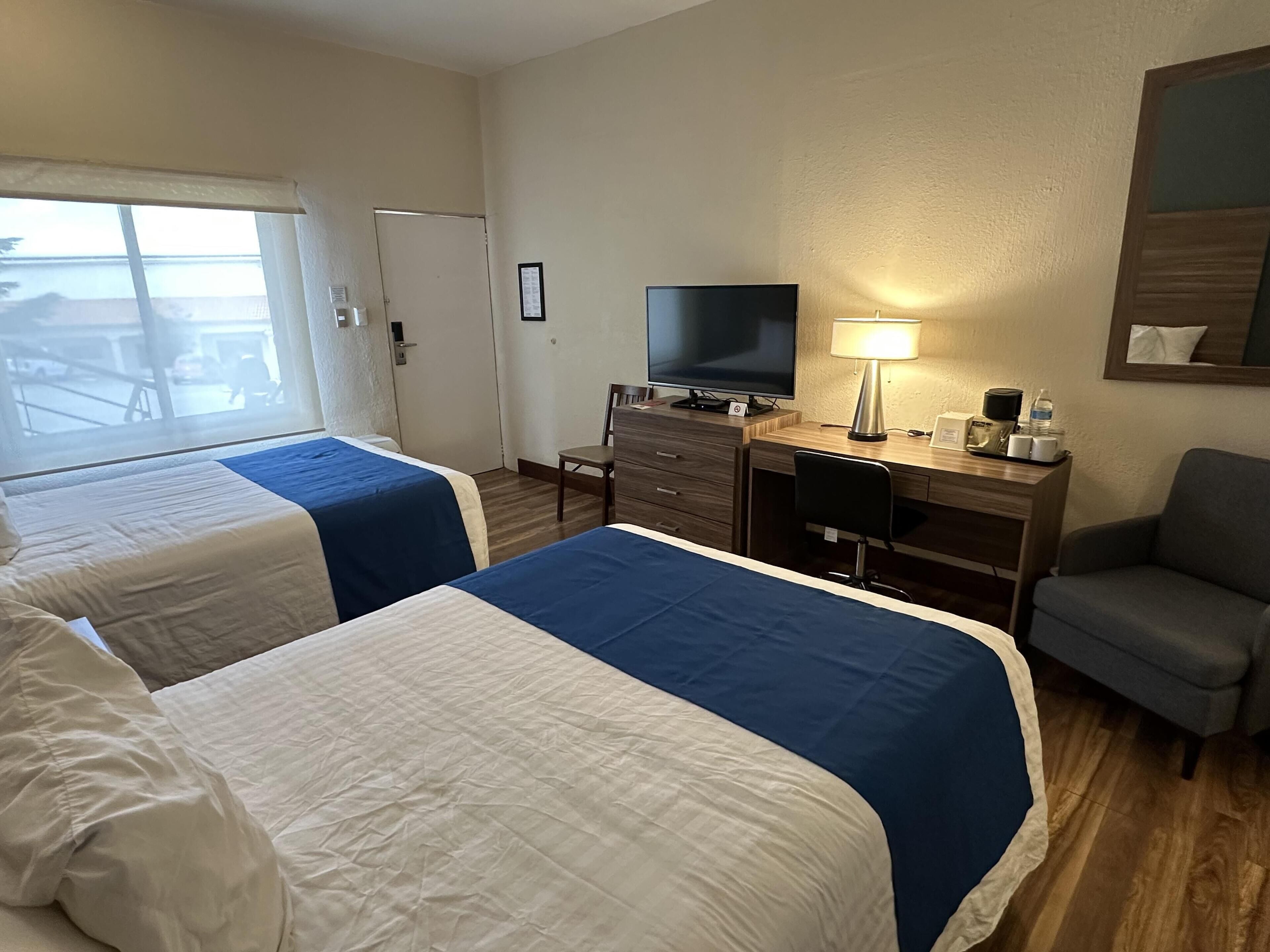 A hotel room with two beds, a desk with a TV, a chair, and a window with a view of the outside.