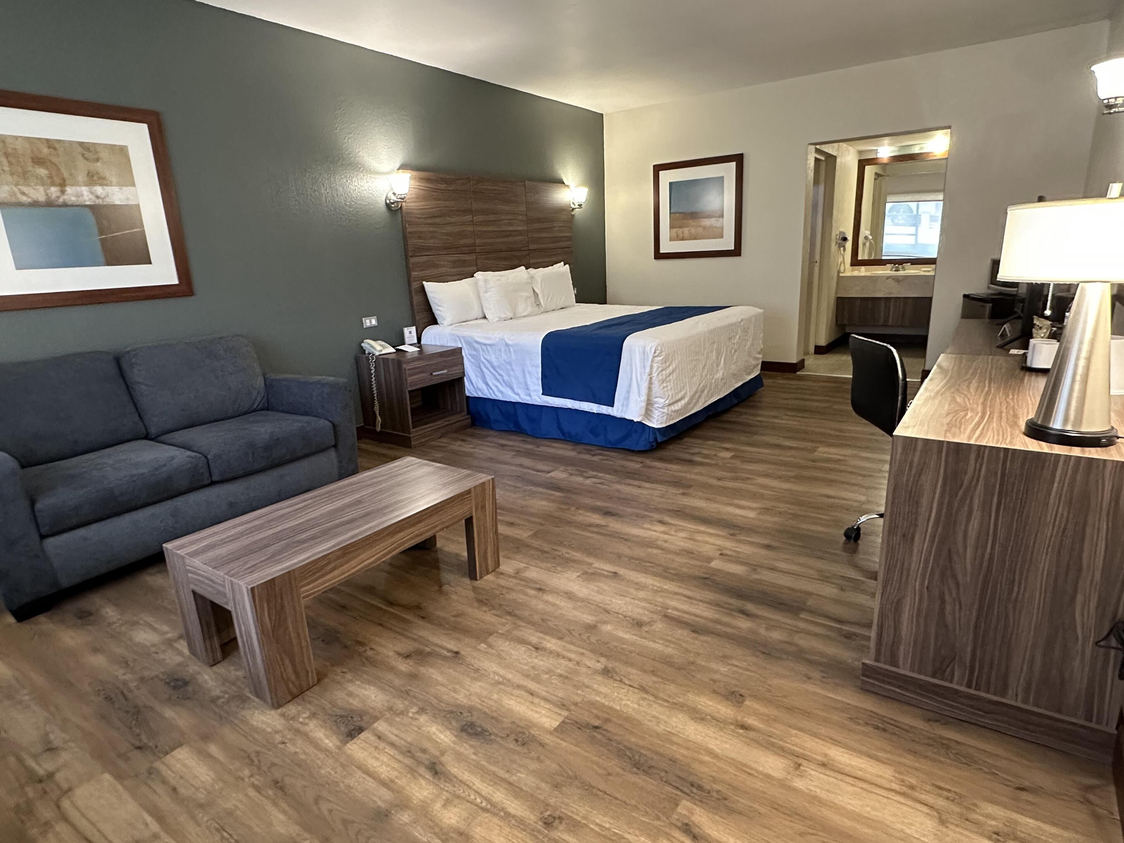 A hotel room with a bed, a desk, a chair, a sofa, and a small table.