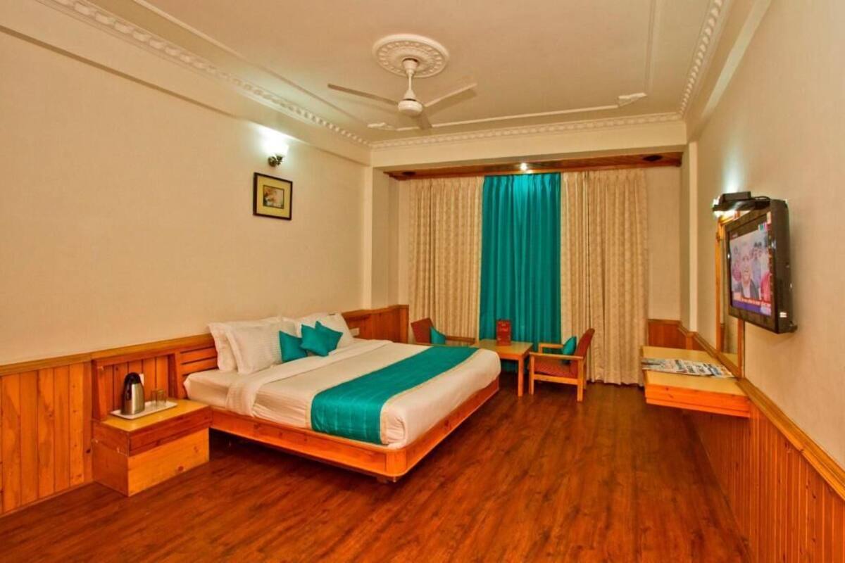 Habitación de hotel con cama, escritorio, silla, televisión y ventilador de techo.