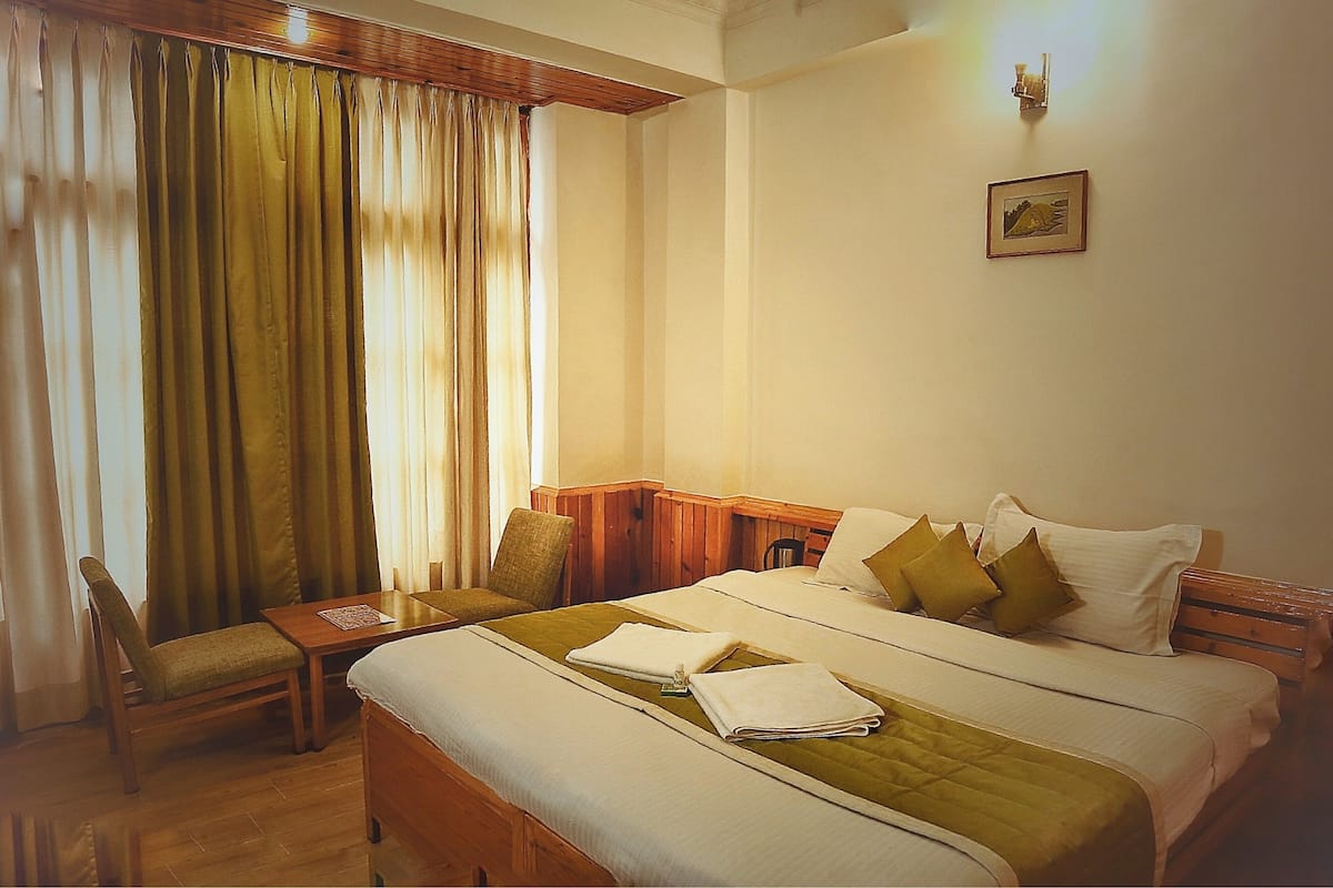 Una habitación de hotel con una cama grande, un cabecero de madera, una mesita pequeña y una silla.