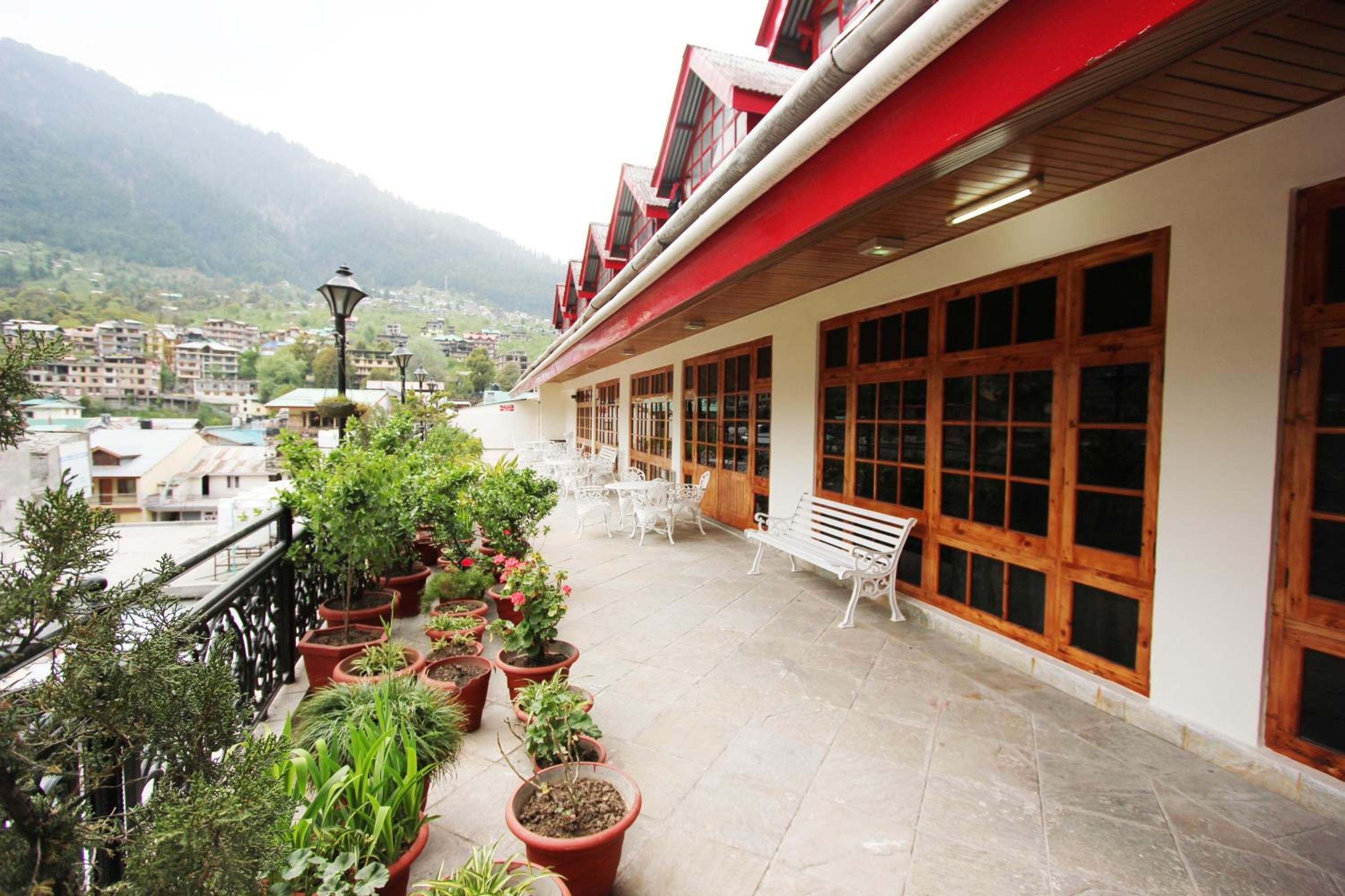 Un balcón de hotel con plantas en macetas, una banca y vistas de los edificios y montañas circundantes.