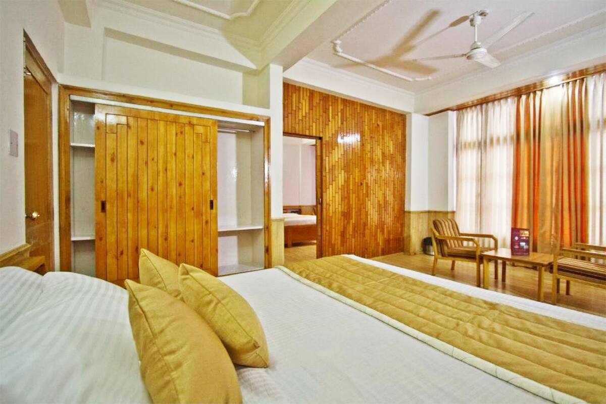 Habitación de hotel con una cama grande, armario de madera, paneles de pared de madera, ventilador de techo y una ventana con cortinas.