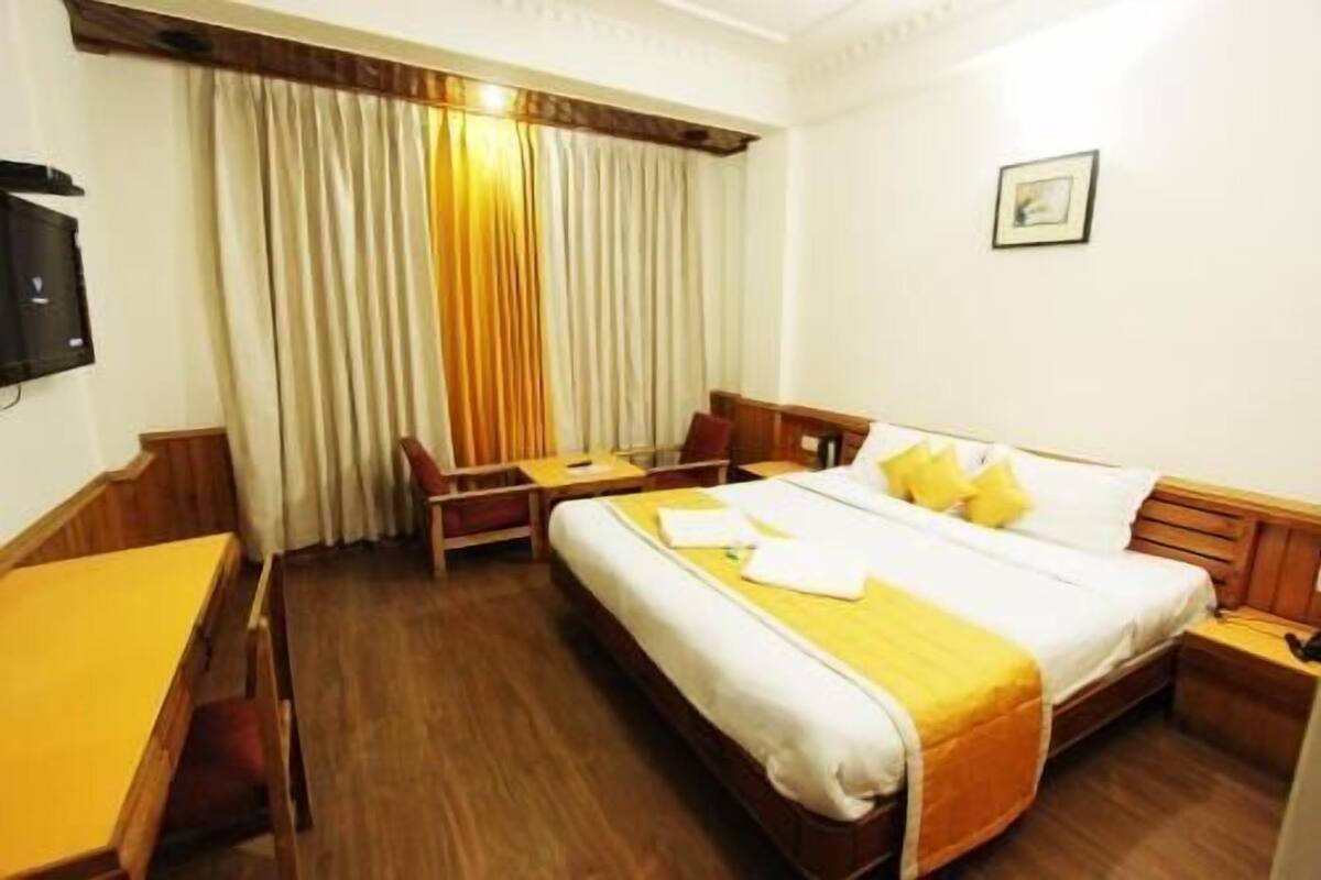 Habitación de hotel con cama, escritorio, silla, televisor y ventana con cortinas.