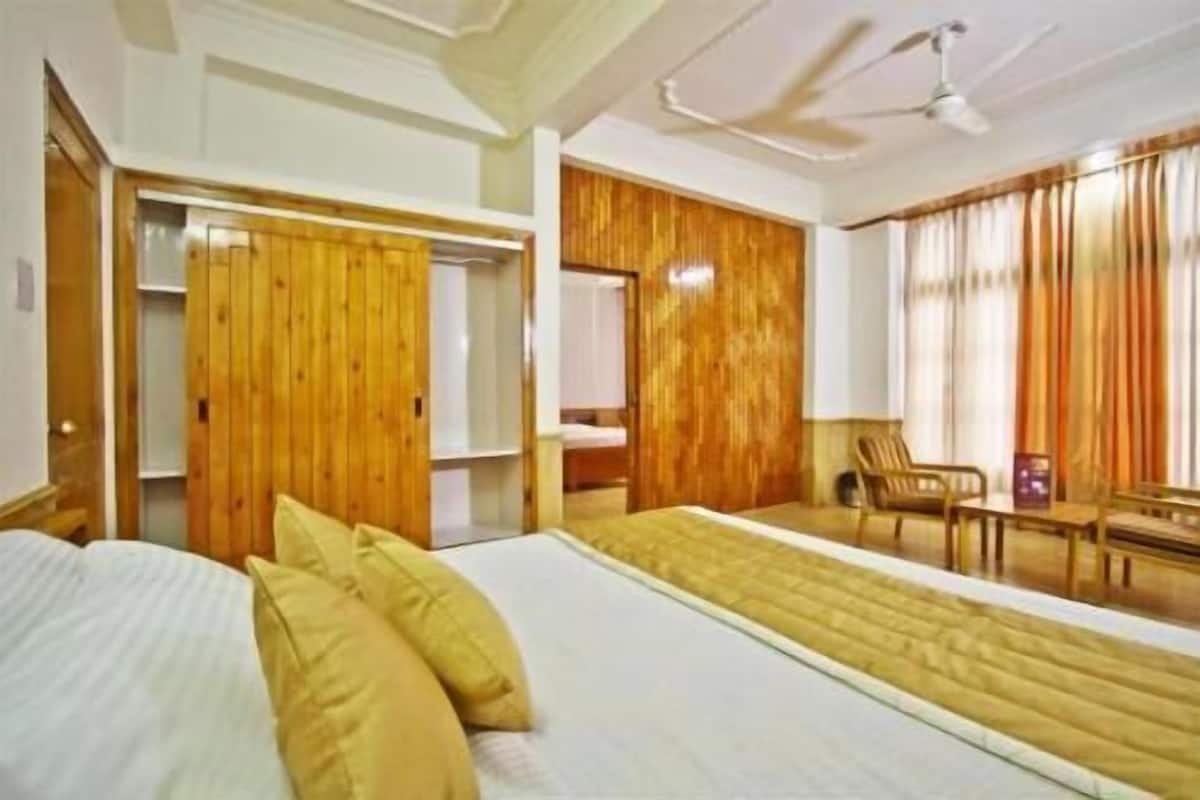 Habitación de hotel con una cama, un armario de madera, un escritorio con una silla y un ventilador de techo.