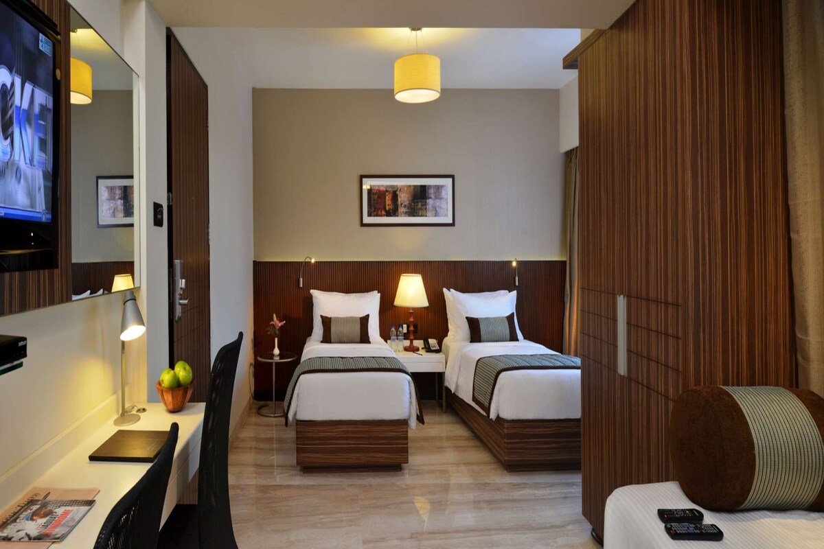 A hotel room with two beds, a desk, a chair, a TV, and a large wooden wardrobe.