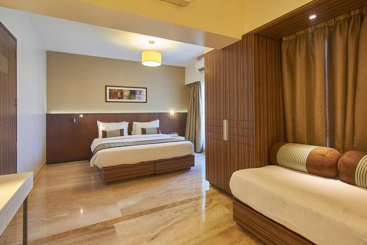 A hotel room with a large bed, a sofa, a wooden wardrobe, and a ceiling light.