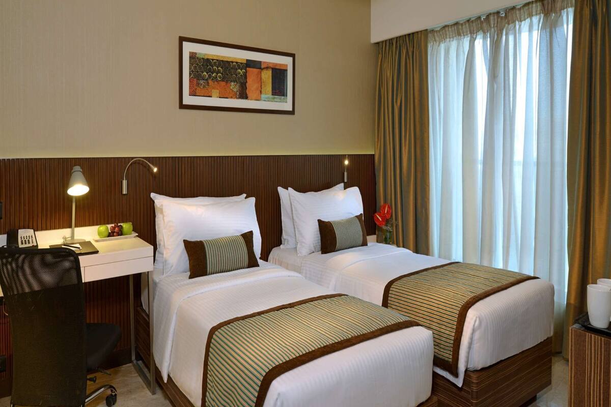 A hotel room with two beds, a desk with a lamp, a phone, and a framed picture on the wall.