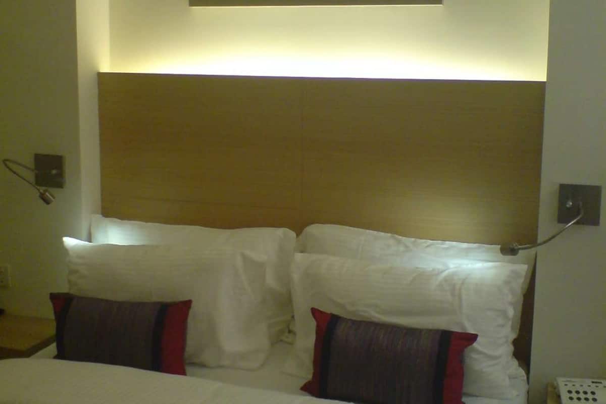 A hotel room with a bed, white bedding, a headboard, and a wall-mounted painting.