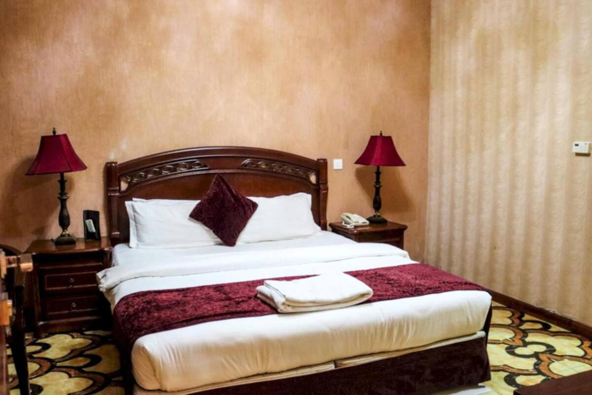 Una cama bien hecha con cabecera de madera, dos lámparas de noche y un suelo estampado.