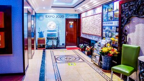 En hotellobby med en blå væg med Expo 2020 Dubai UAE logo, et receptionsskrank, en grøn stol og en væg med diverse souvenirs.