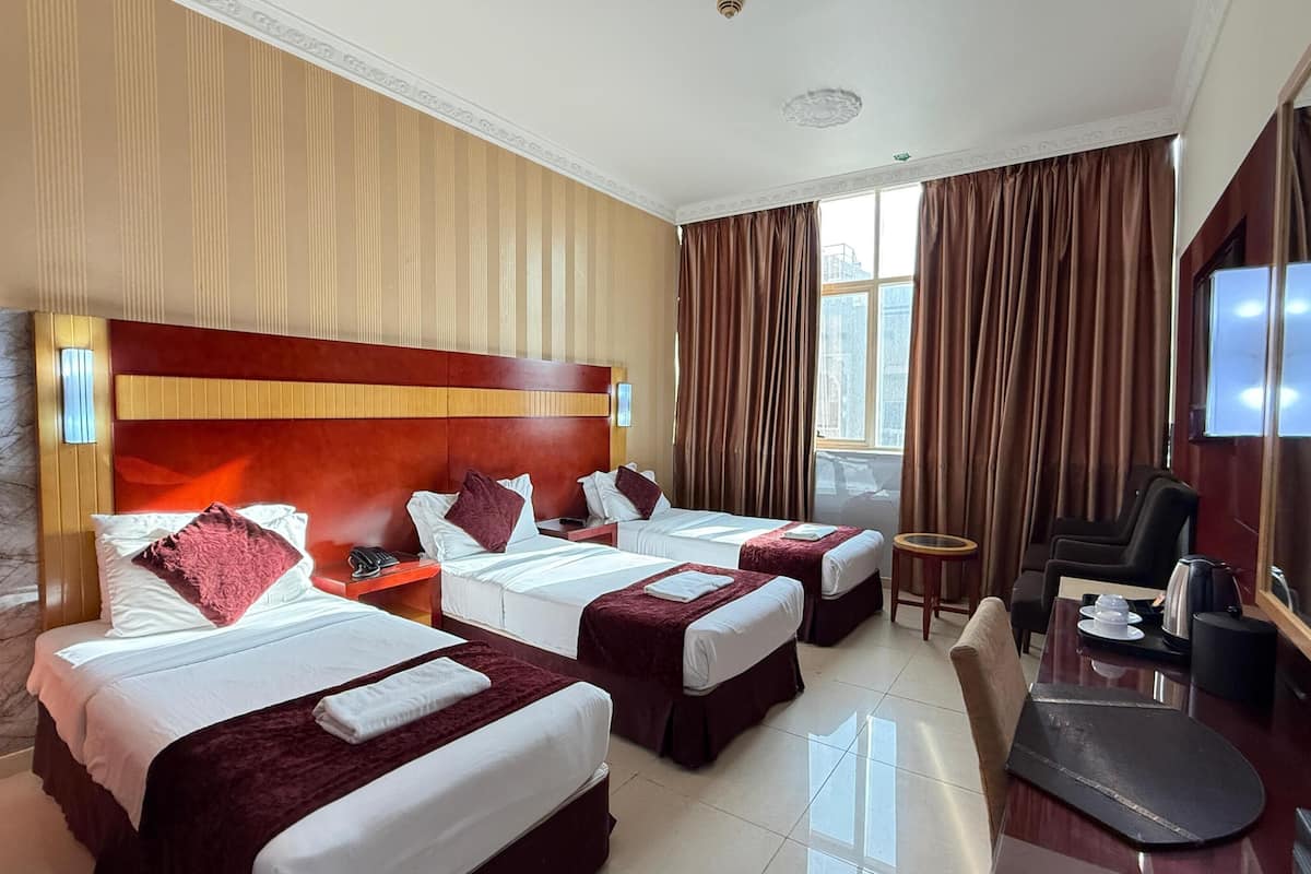 Habitación de hotel con dos camas, un escritorio, una silla, un televisor y un ventanal con cortinas.