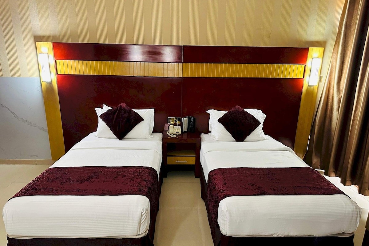 Habitación de hotel con dos camas, cada una con cabecera, mesita de noche y lámpara.