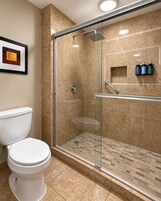 A modern bathroom with a glass-enclosed shower, a white toilet, and a framed picture on the wall.