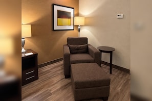 Habitación de hotel con sofá, reposapiés, una mesita, lámpara, un cuadro en la pared y un termostato.