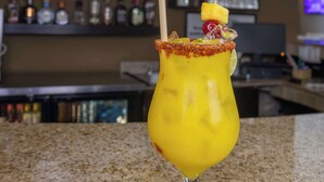 Zona de bar con mostrador, un televisor mostrando un noticiero y varias botellas de licores en estantes.