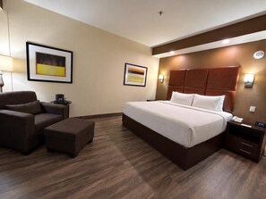 Ein Hotelzimmer mit einem großen Bett, einem Sessel, einem kleinen Tisch und zwei Wandlampen.