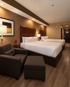 Una habitación de hotel con una cama, dos mesitas de noche, una lámpara, una silla y un pequeño reposapiés.