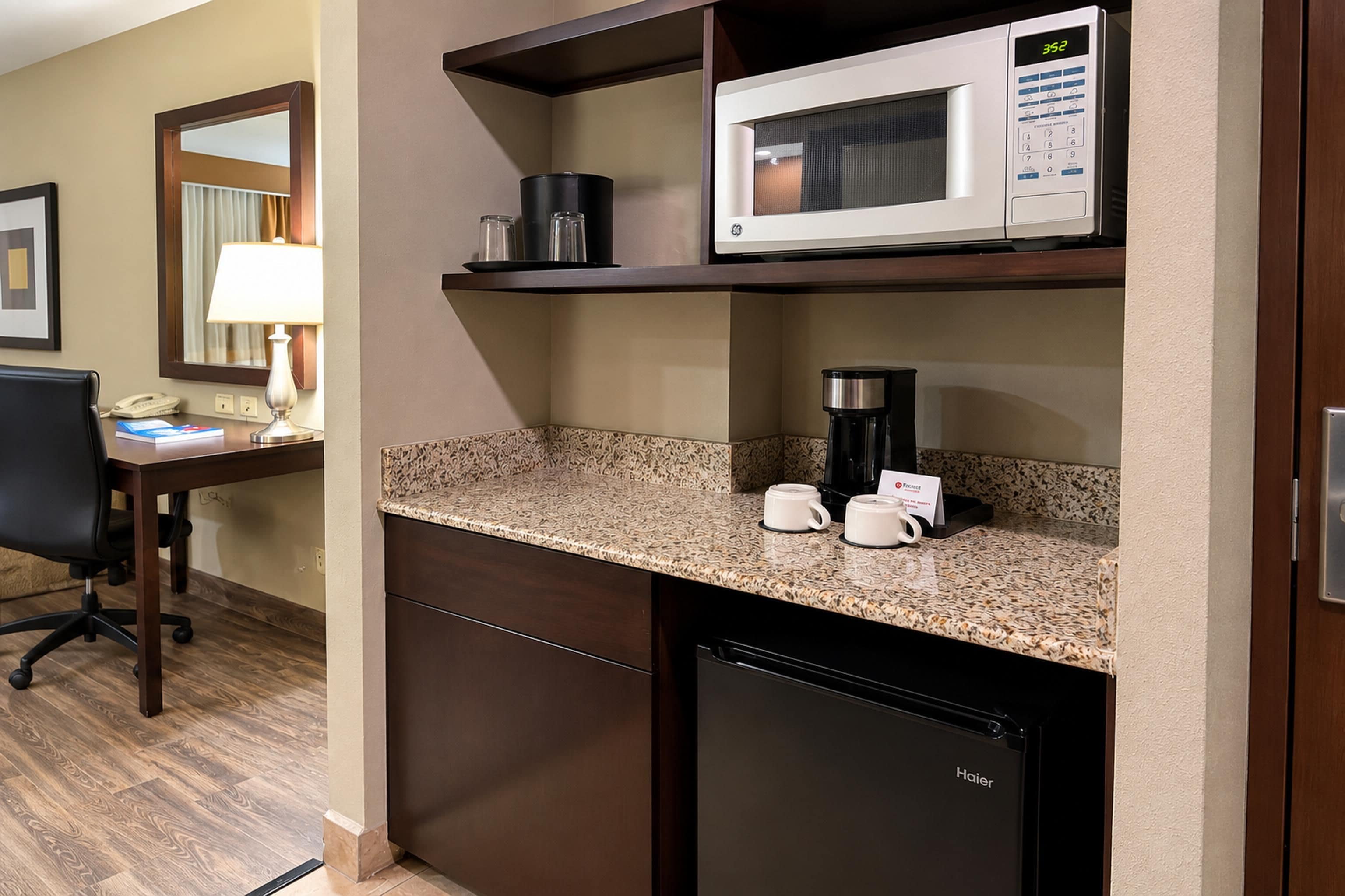 Una kitchenette con microondas, cafetera y tazas de café sobre la encimera.