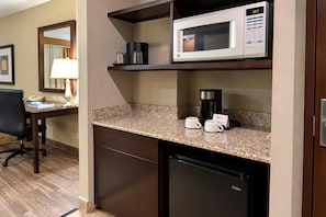 Una kitchenette con microondas, cafetera y tazas de café sobre la encimera.
