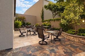 Un espace extérieur aménagé en terrasse, avec plusieurs tables et chaises, entouré de plantes et d’un mur en pierre.