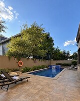 A swimming pool with a waterfall feature, surrounded by lounge chairs and a tree.