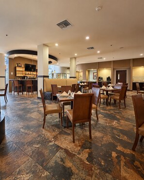 Een ruim restaurant met meerdere eettafels en stoelen, een bar en een zithoek met comfortabele banken.