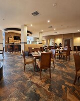 Un restaurante espacioso con numerosas mesas y sillas, una zona de bar y un área de estar con bancos acolchados.