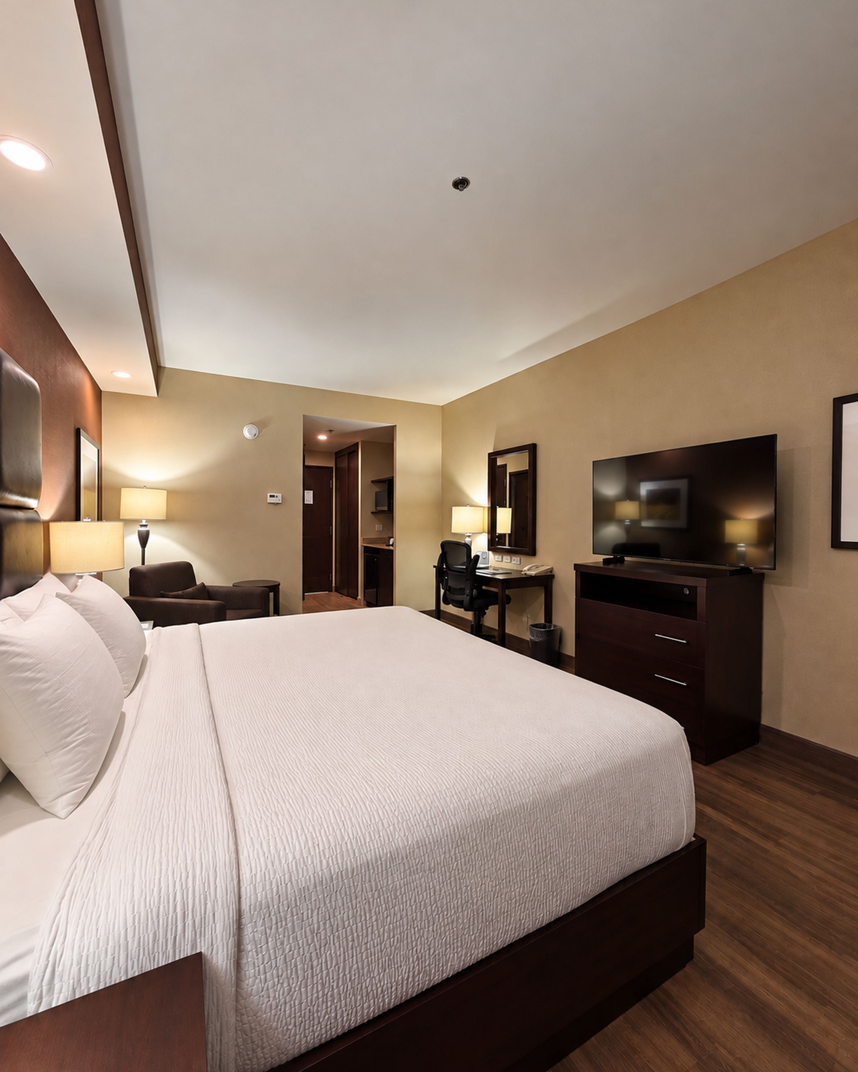 A hotel room with a large bed, a desk, a television, and a bathroom visible through an open door.