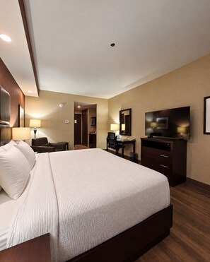 Habitación de hotel con una cama grande, un escritorio, un televisor y un baño visible a través de una puerta abierta.