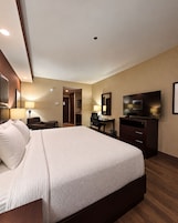 Habitación de hotel con una cama grande, un escritorio, un televisor y un baño visible a través de una puerta abierta.