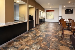 Un vestíbulo de hotel con una larga recepción, una estación de café y un comedor con mesas y sillas.