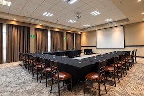 Une salle de conférence avec une longue table, des chaises, un écran de projection et des rideaux.