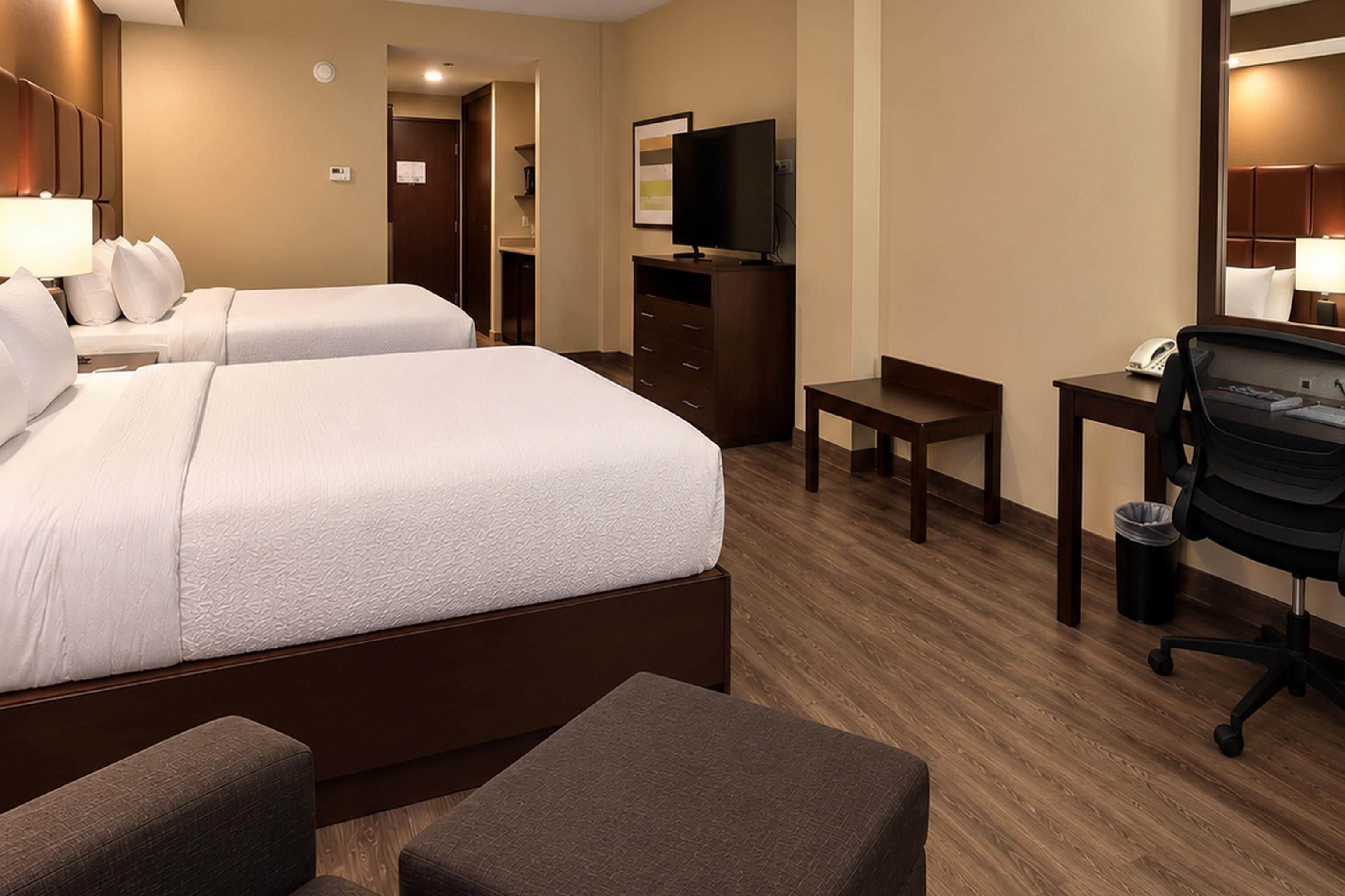 Een hotelkamer met twee bedden, een bureau, een stoel, een televisie en een prullenbak.