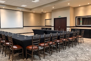 Ein Konferenzraum mit einem langen Tisch, Stühlen, einer Projektionsleinwand und Teppichboden.