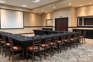 A conference room with a long table, chairs, a projector screen, and a carpeted floor.