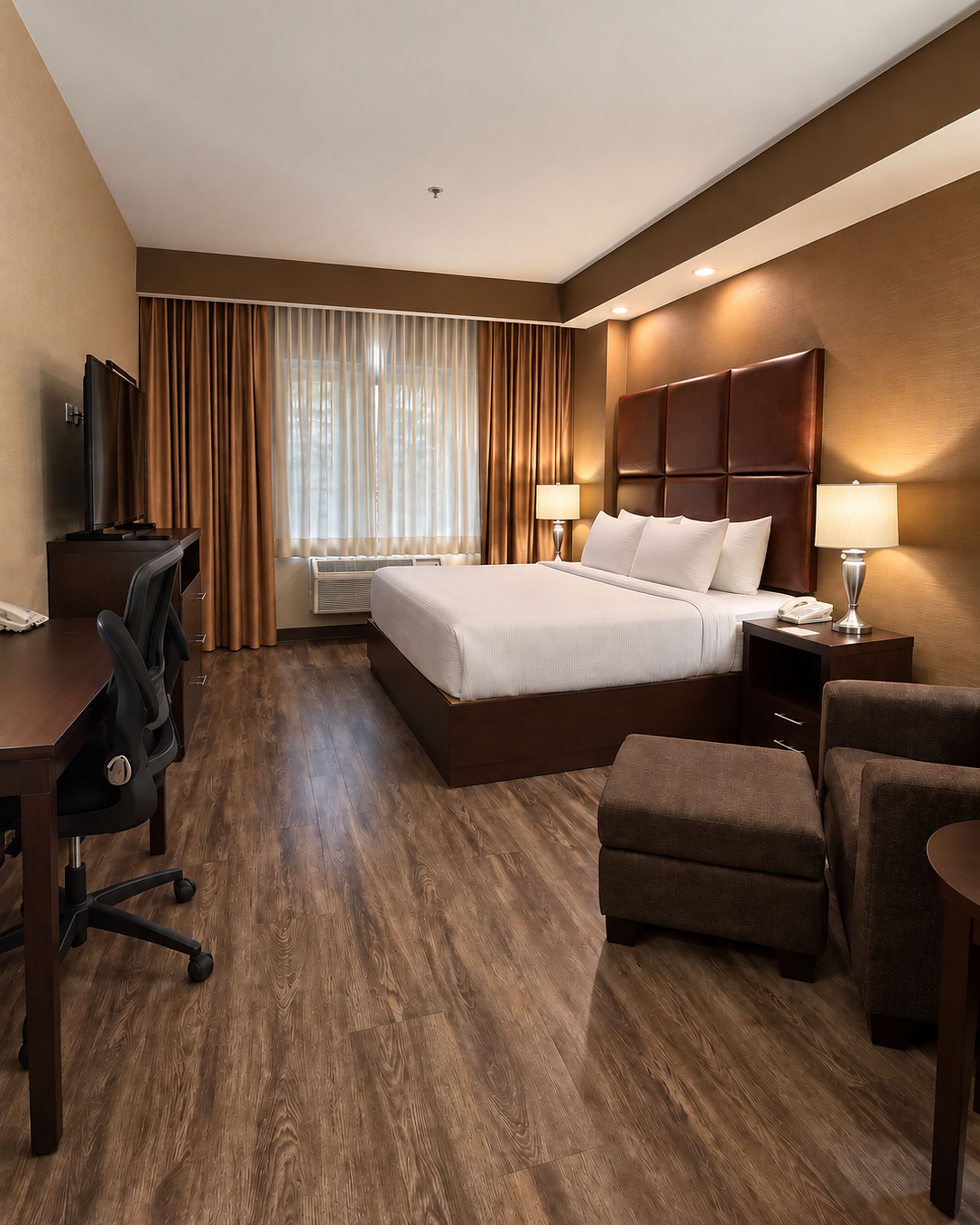 Une chambre d’hôtel avec un grand lit, un bureau avec une chaise, une petite table avec une lampe et un canapé.
