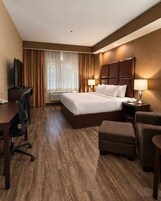 Quarto de hotel com uma cama grande, uma escrivaninha com cadeira, uma mesa pequena com abajur e um sofá.