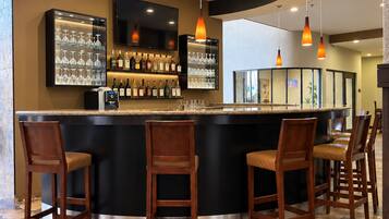 A bar area with a curved counter, multiple bar stools, a television mounted above the bar, and a variety of bottles and glasses on shelves.