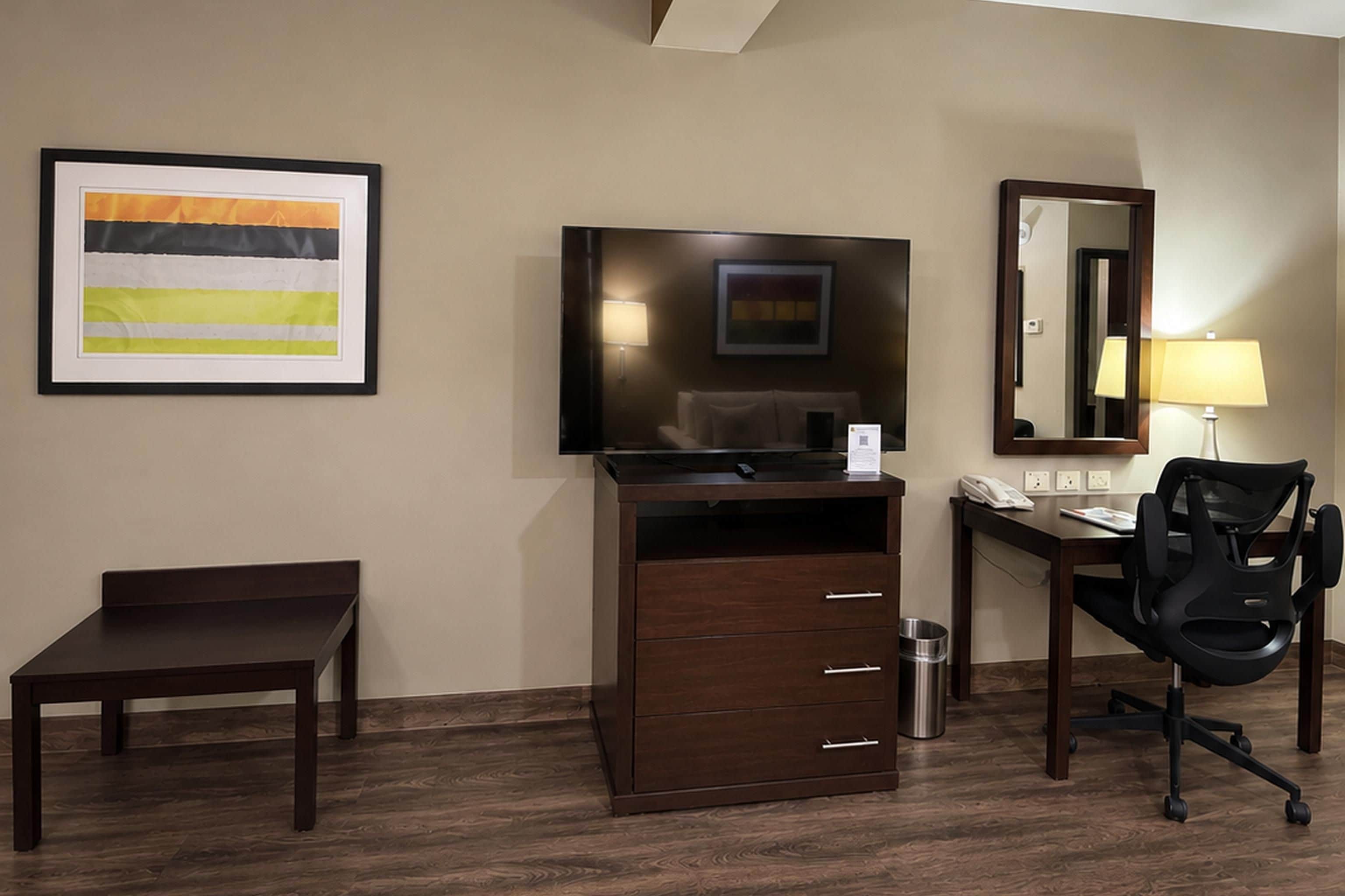 A hotel room with a desk, chair, TV, and a framed abstract painting.