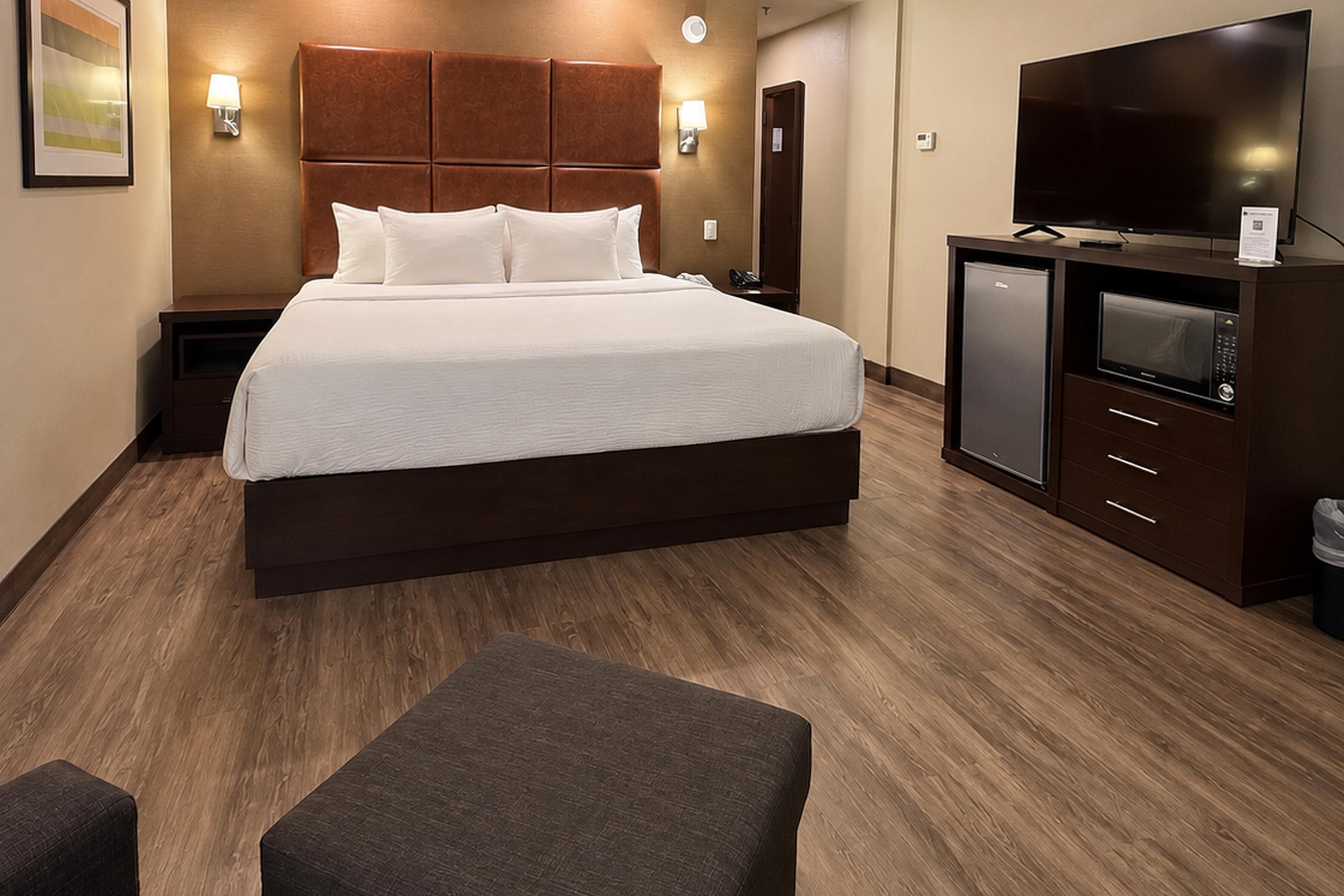 A hotel room with a large bed, a television, a minibar, and a desk.