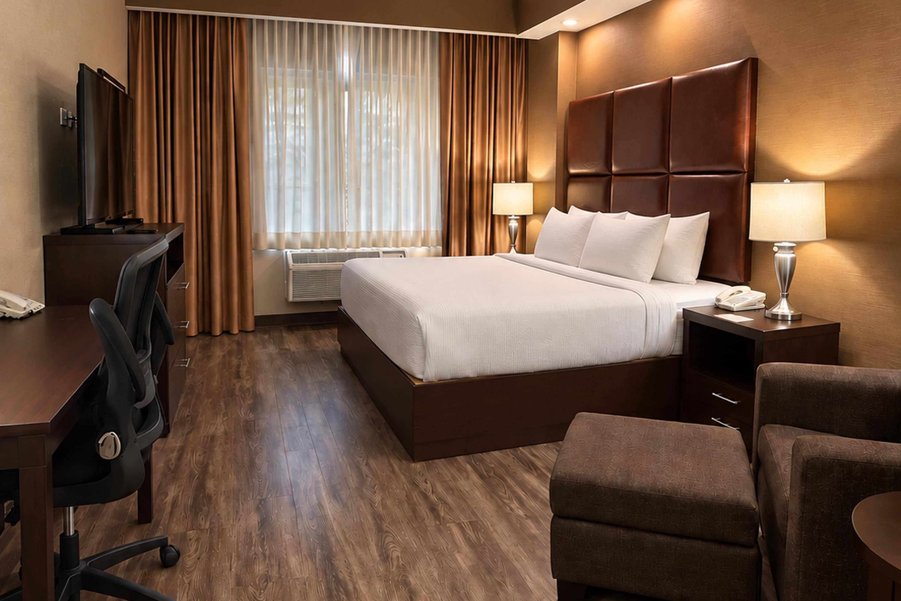 Una habitación de hotel con una cama grande, un escritorio, una silla, un televisor y una ventana con cortinas.
