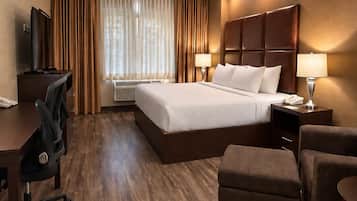 Una habitación de hotel con una cama grande, un escritorio, una silla, un televisor y una ventana con cortinas.