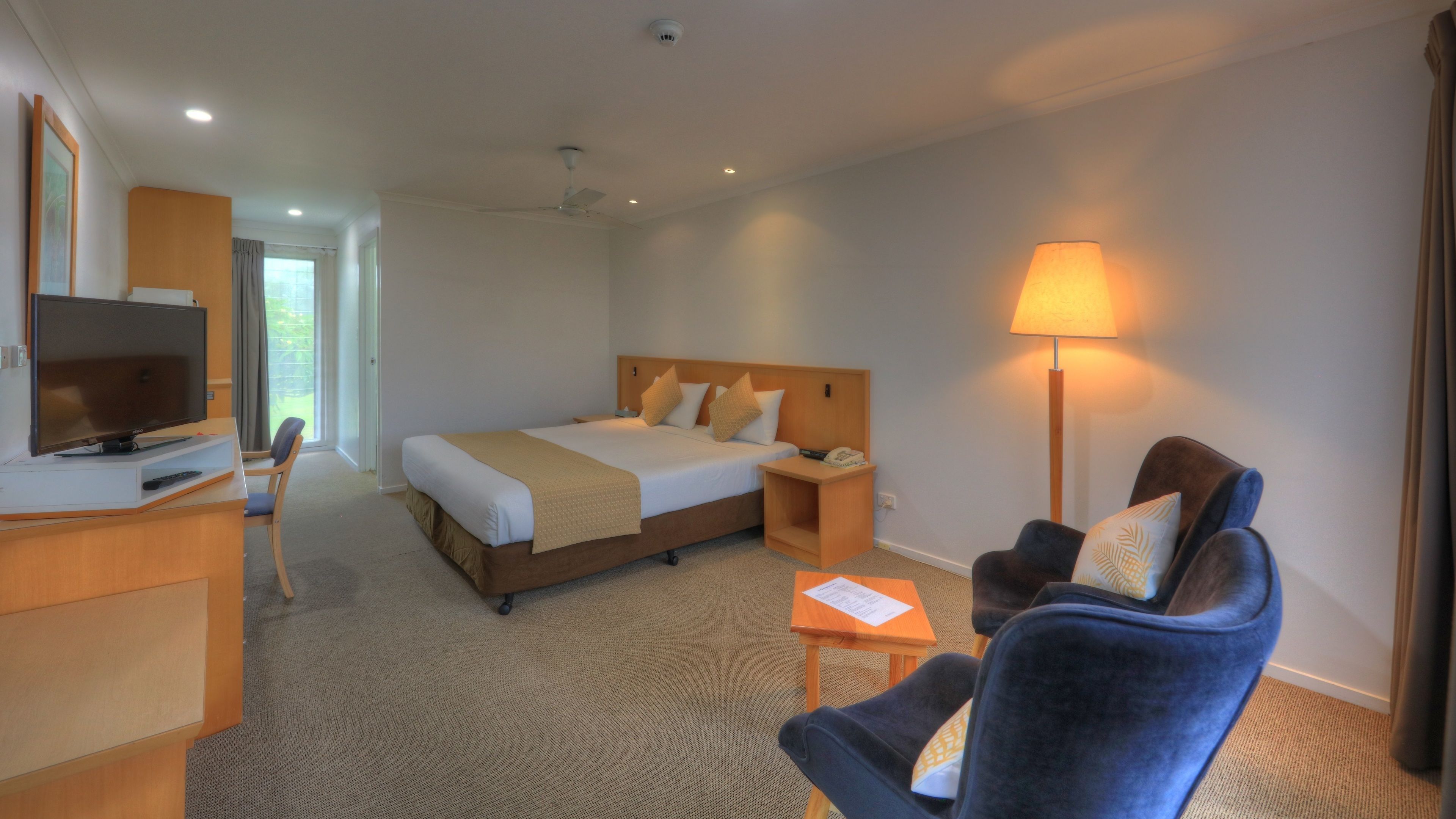 A hotel room with a bed, bedside table, lamp, TV, and a chair.