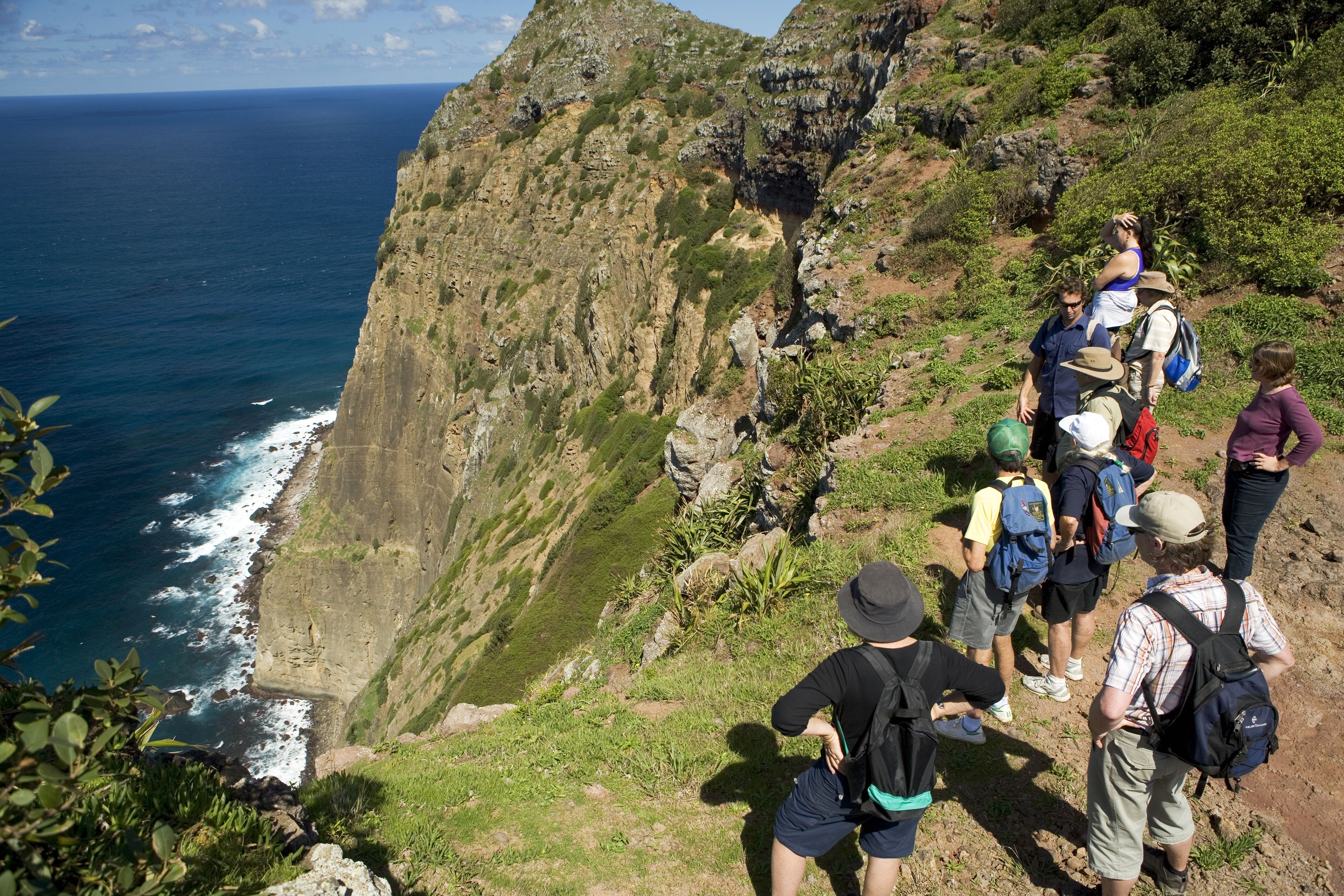 A group of people hiking on a rocky cliff with a view of the ocean.