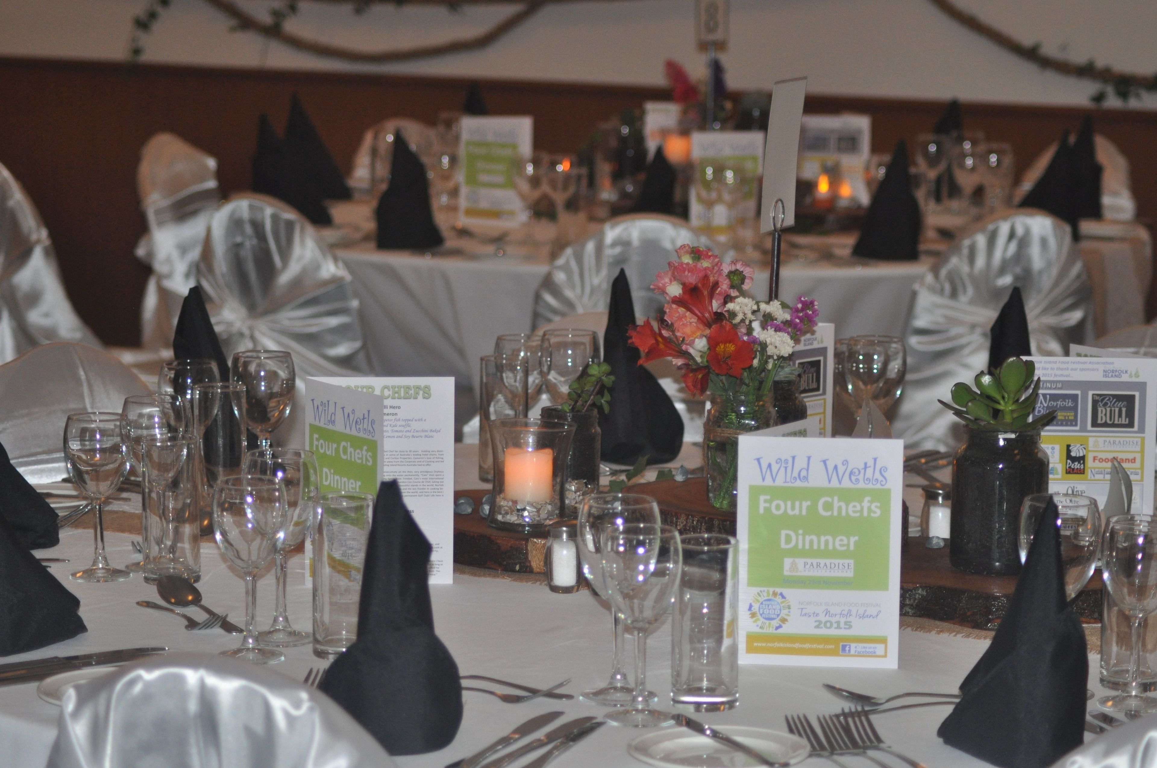 A formal dining table set for a four-chef dinner at Wild Wetts Paradise, complete with glassware, napkins, and floral centerpieces.