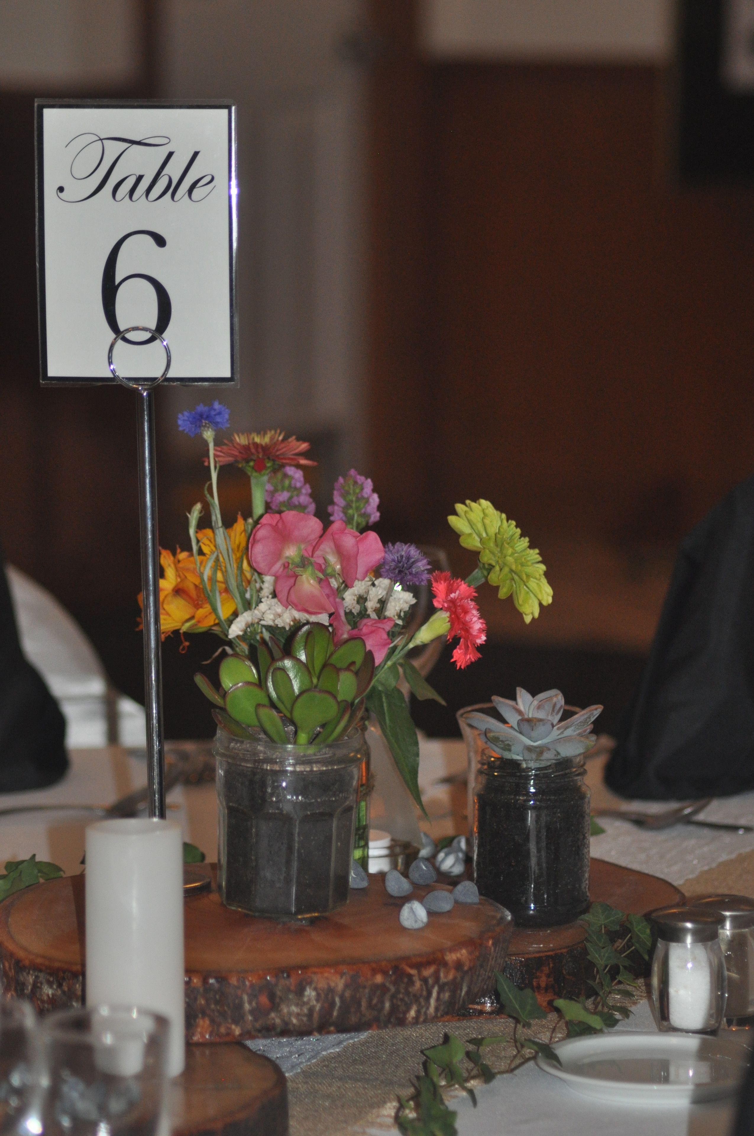 Een gedekte tafel met een bord waarop 'Tafel 6' staat, een bloemstuk en een kandelaar.